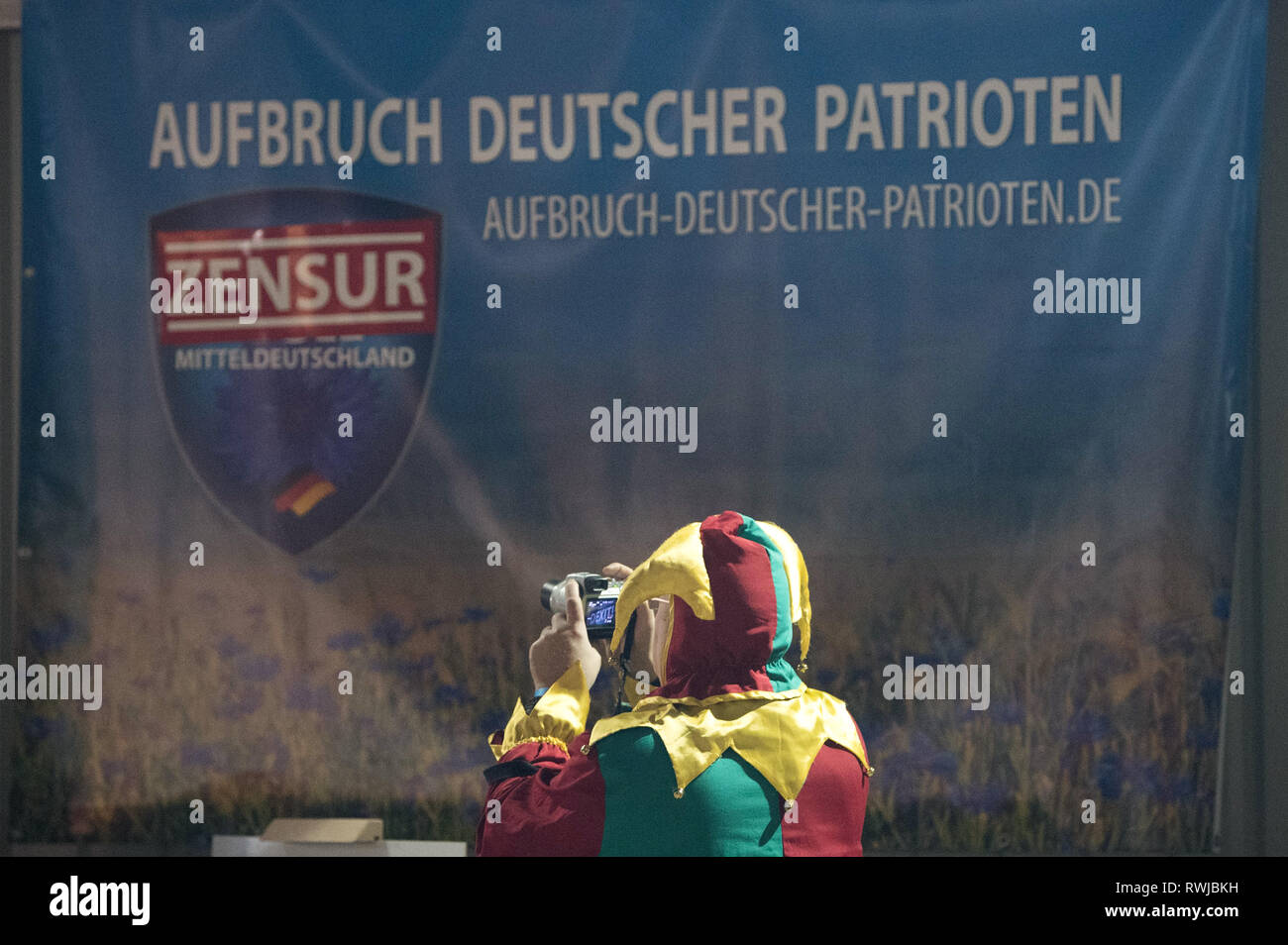 Bahretal, Germany. 06th Mar, 2019. A man in a harlequin costume is standing in front of an AdP poster at the Ash Wednesday event of the party Aufbruch deutscher Patrioten (AdP). Credit: Sebastian Kahnert/dpa/Alamy Live News Stock Photo