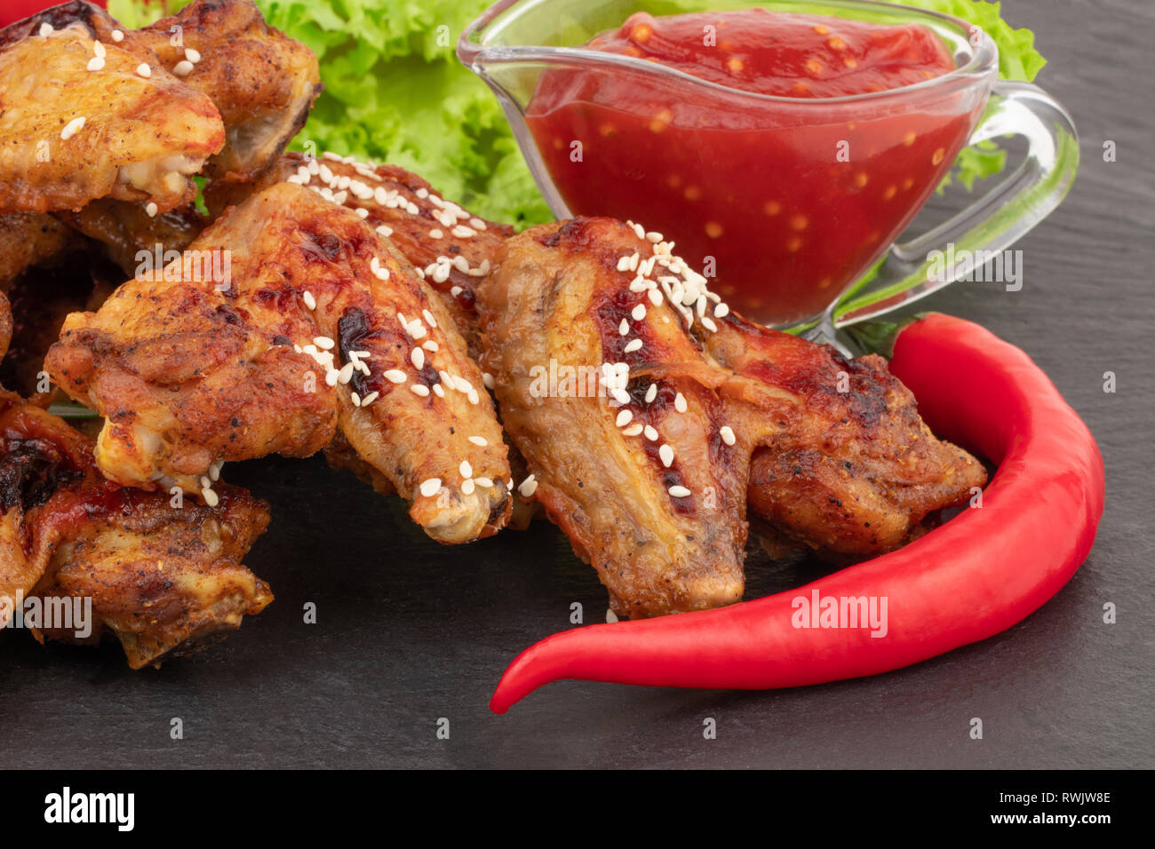 Baked chicken wings with sesame seeds and sweet chili sauce on dark