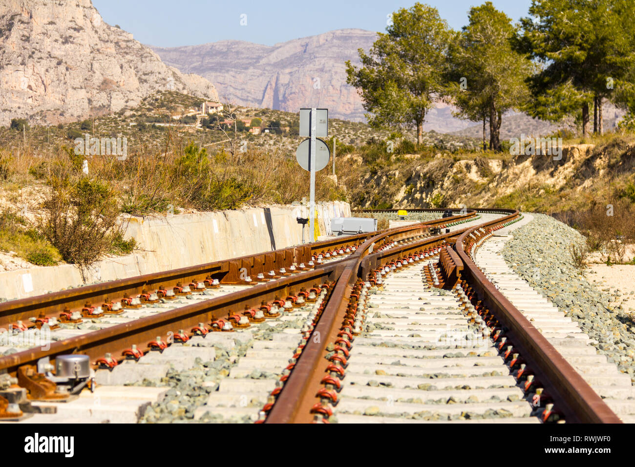 A railroad switch track with traffic signs, mountains and trees in the background Stock Photo