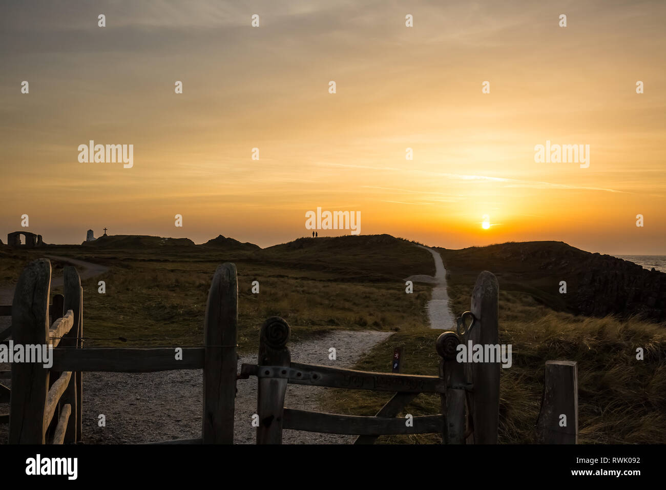 Golden winter sunset, Llanddwyn Island, Anglesey. View of coastal path along peninsula sunlit wooden gates in foreground, naturally lit by setting sun. Stock Photo