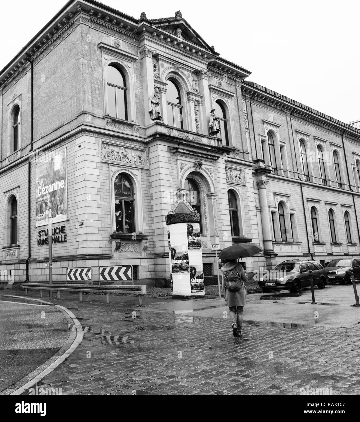 Karlsruhe, Germany - Oct 29, 2017: Young woman with umbrella walking toward Staatliche Kunsthalle Karlsruhe State Art Gallery on Hans-Thoma-Strasse street - black and white Stock Photo