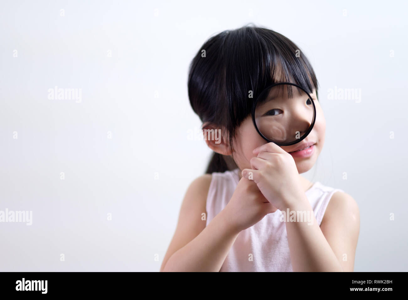 Little girl child looking through a magnifying glass on white background Stock Photo