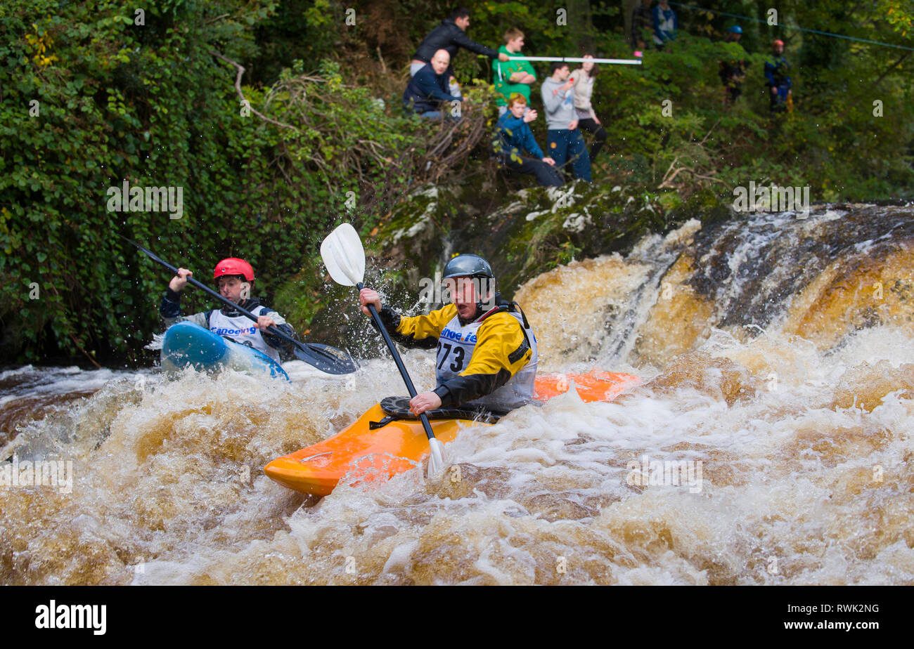 Kayaks race down rapids with spectators watching from the shoreline at