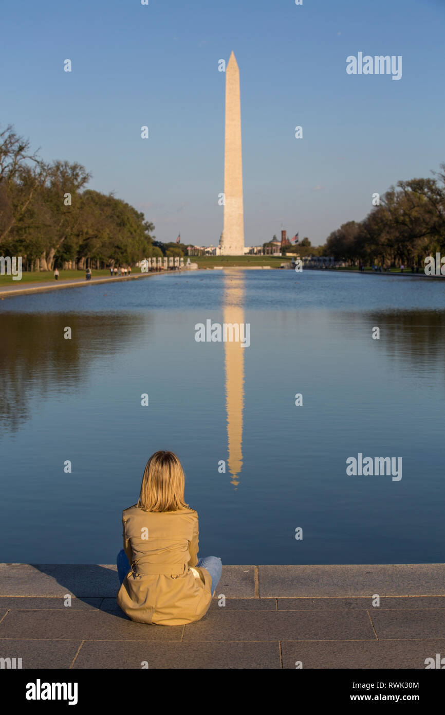 Tourist sitting at water's edge of reflecting pool viewing Washington Monument, taken from Lincoln Monument; Washington D.C., United States of America Stock Photo