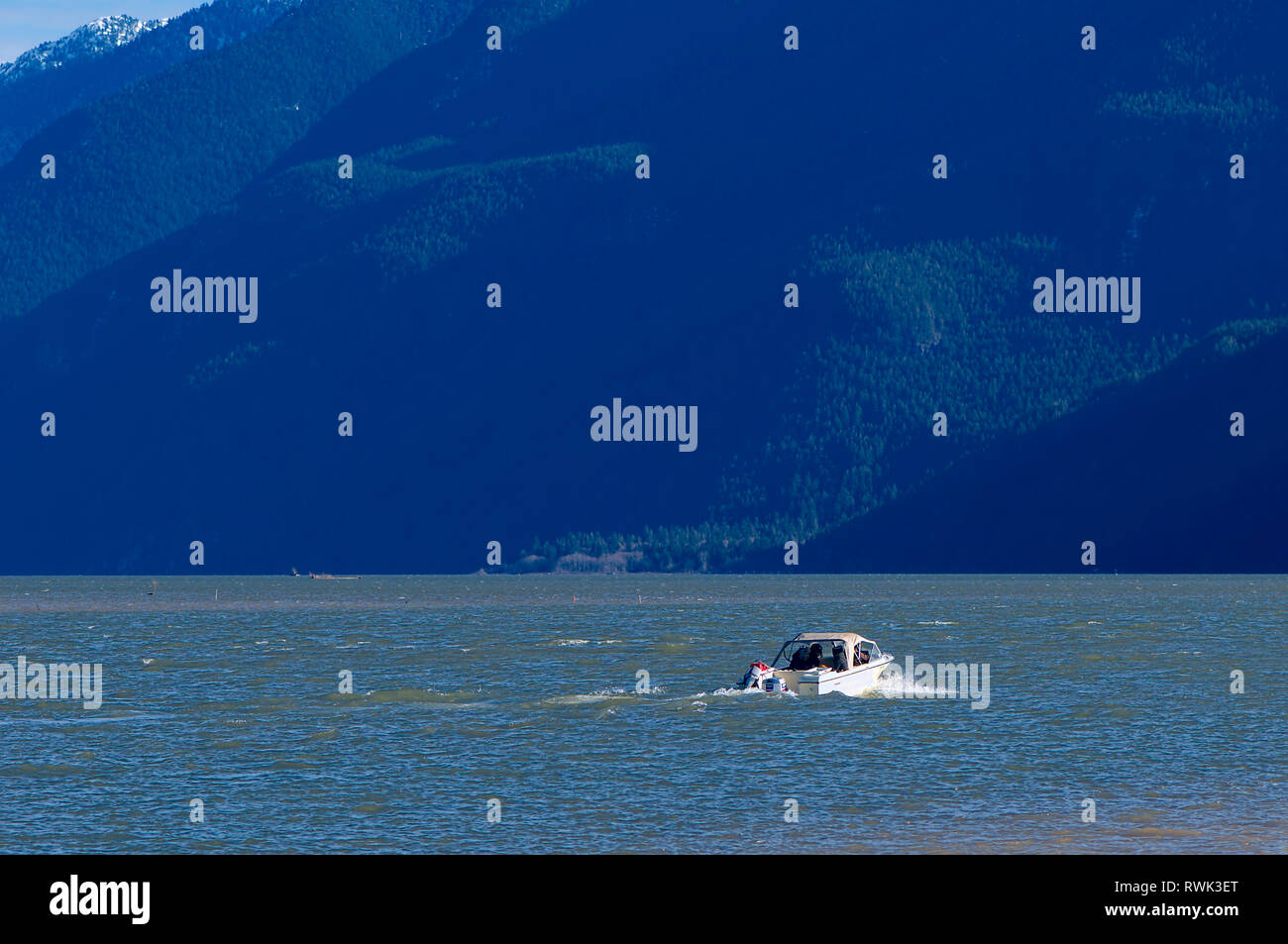 A single boat traveling on Pitt Lake with the dark side of a mountain looming in the background. Pitt Meadows, British Columbia, Canada Stock Photo