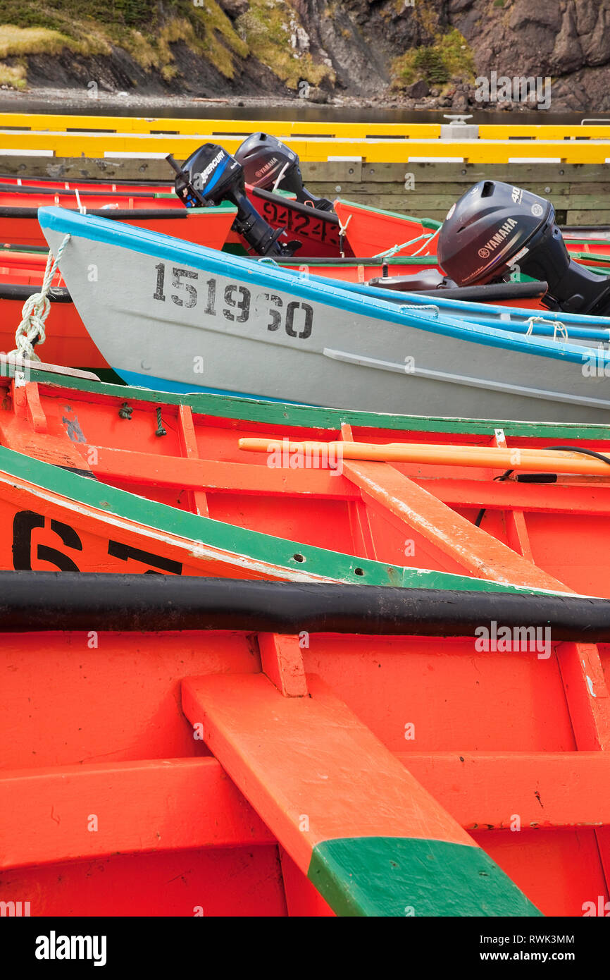 Colour pattern of orange, green, blue and yellow created by a row of Lark Harbour dories (with the exception of the white one) on a slipway next to the wharf at Bottle Cove, Newfoundland, Canada Stock Photo