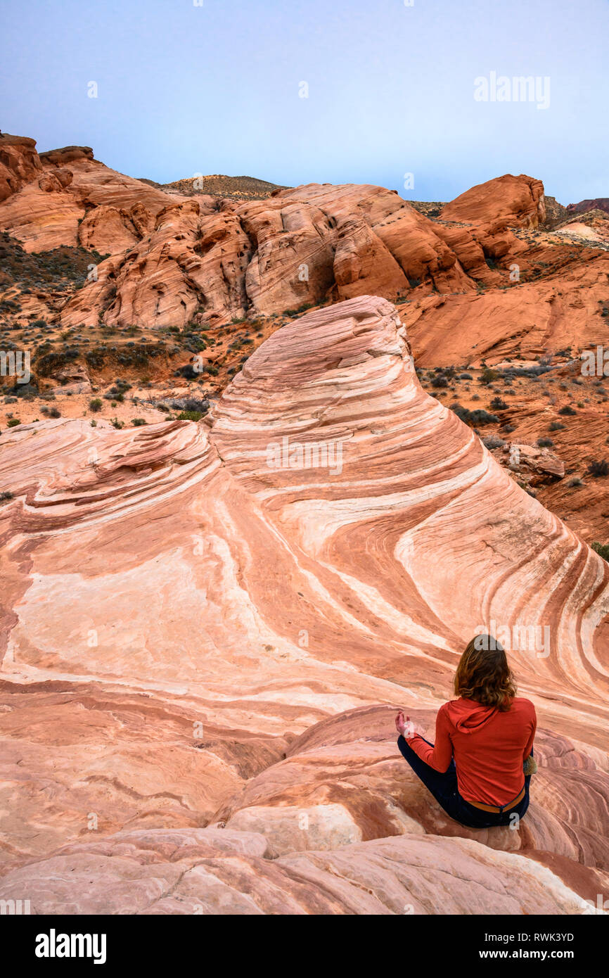 Woman sitting in meditation pose at the Fire Wave sandstone rock formation in Valley of Fire State Park, Nevada. Stock Photo