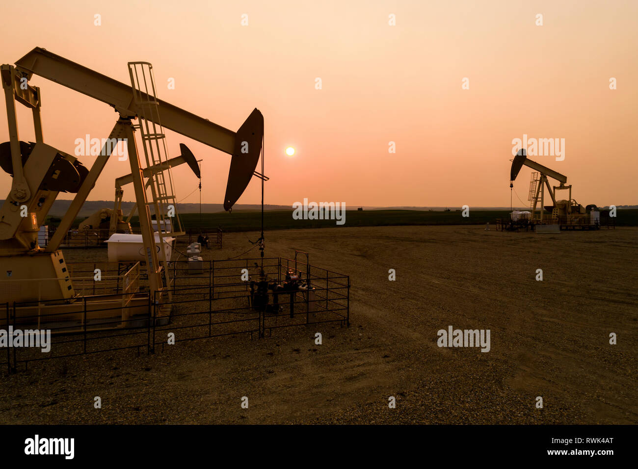 High view of several pumpjacks at sunset with a warm glowing sun ball, West of Airdrie; Alberta, Canada Stock Photo