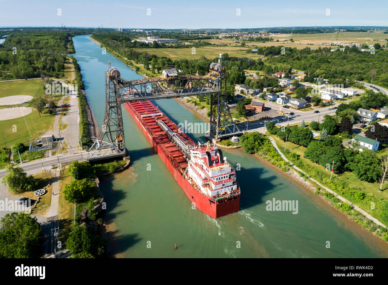 Aerial view of large laker ship navigating under a metal lift bridge in a canal with blue sky; Thorold, Ontario, Canada Stock Photo