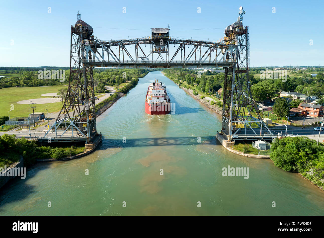 Aerial view of large laker ship navigating under a metal lift bridge in a canal with blue sky; Thorold, Ontario, Canada Stock Photo