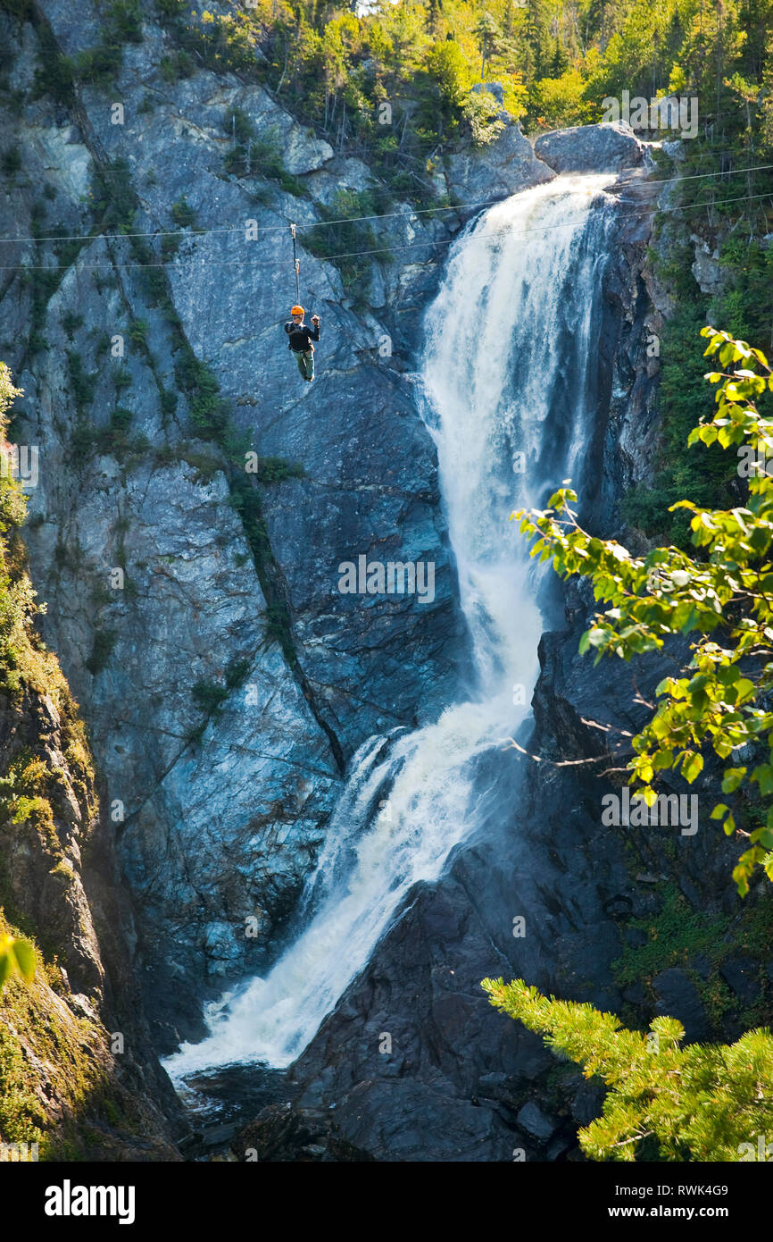 Zip liner traversing past Steady Brook Falls at Marble Mountain Resort near Corner Brook, Newfoundland, Canada. The operation is run by Marble Zip Tours Stock Photo