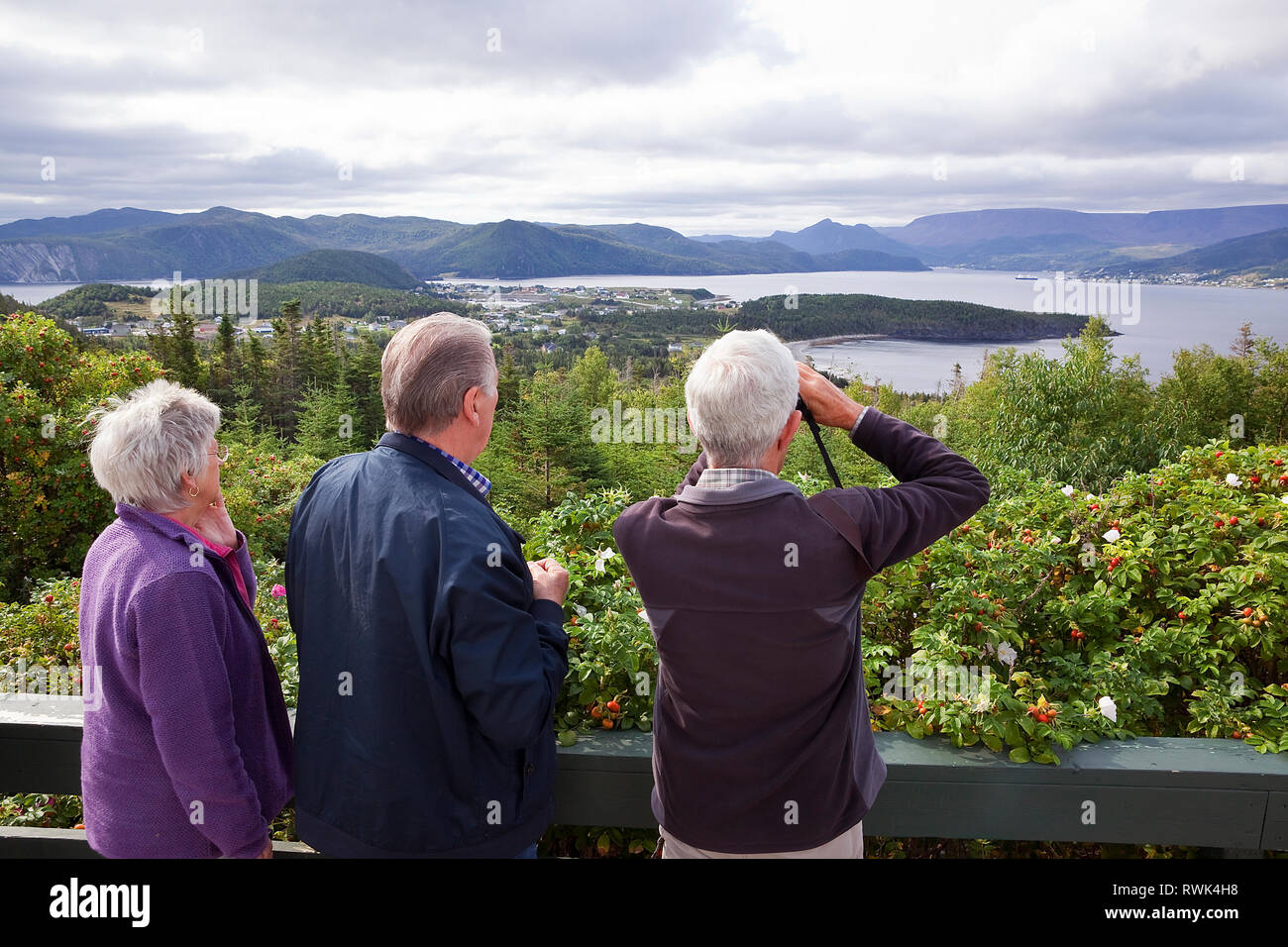 Three mature adults admiring the view from a lookout located at Jenniex Heritage House in Norris Point. In view encompasses the town of Norris Point, Bonne Bay and Gros Morne National Park, Western Newfoundland, Canada Stock Photo