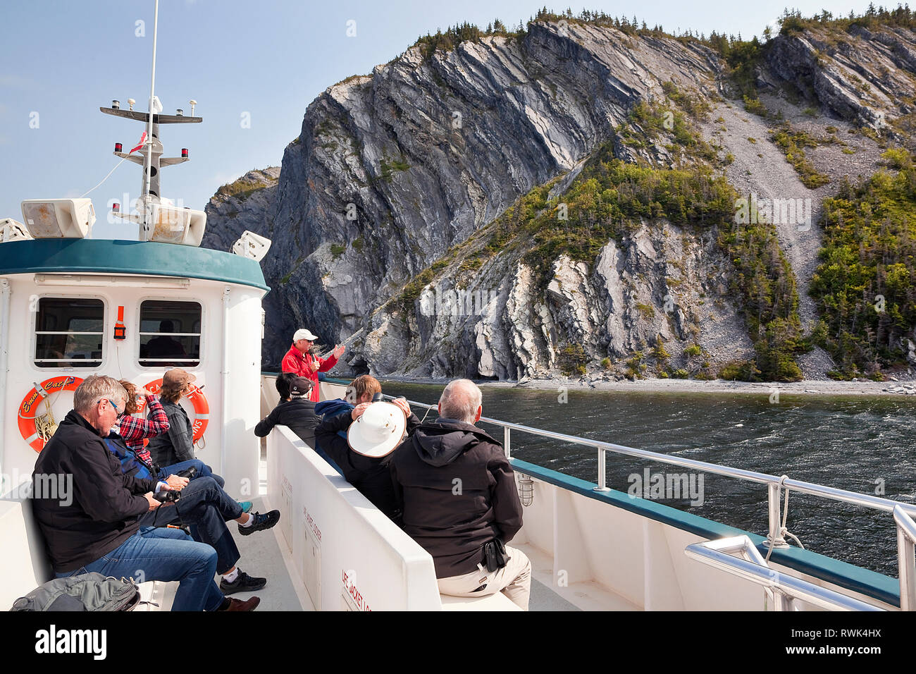 Tour boat guide and passengers approaching Shag Cliff off the southen end of Norris Point and within Gros Morne National Park, Newfoundland, Canada Stock Photo