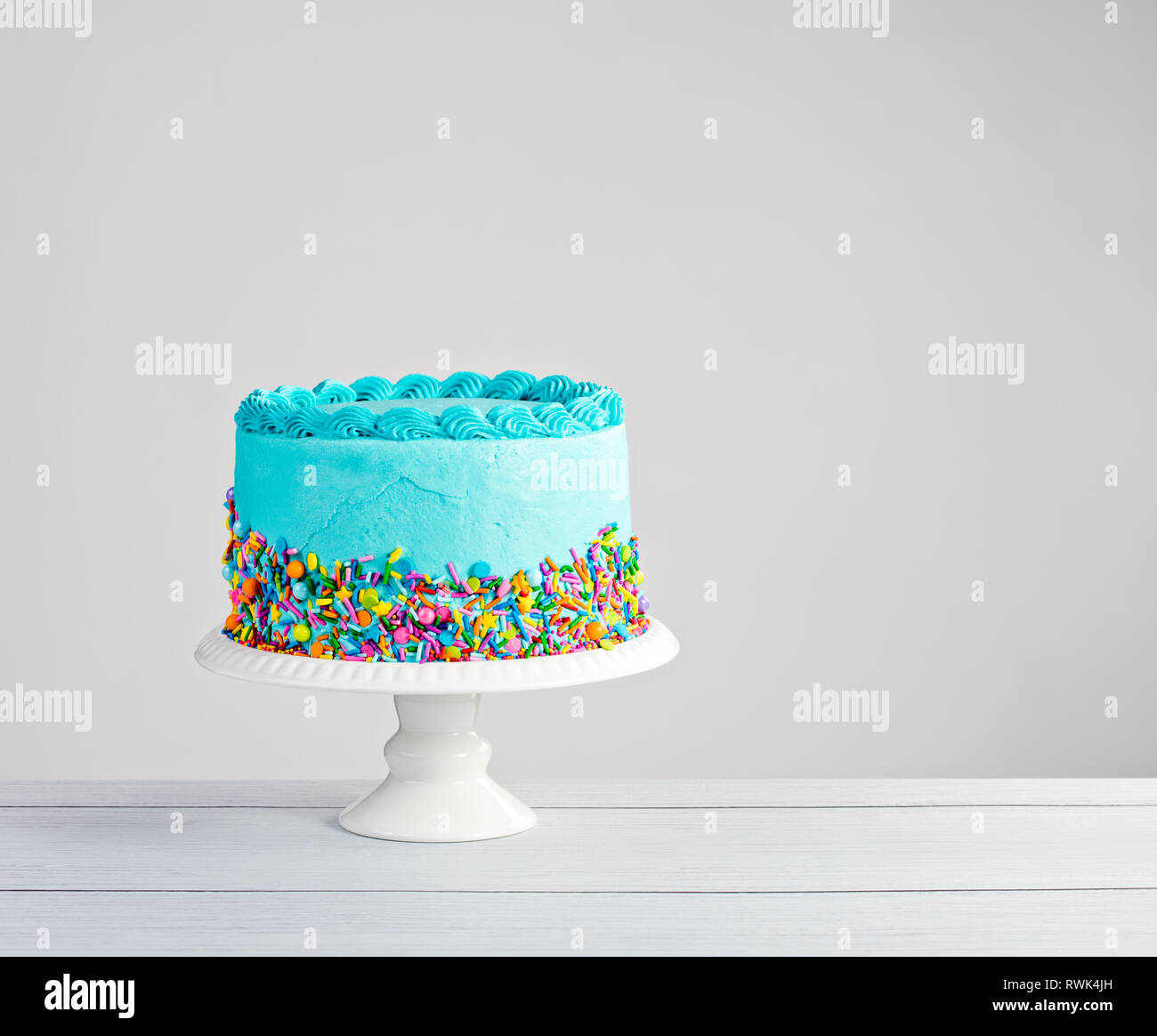Blue buttercream cake with colorful sprinkles over a light grey