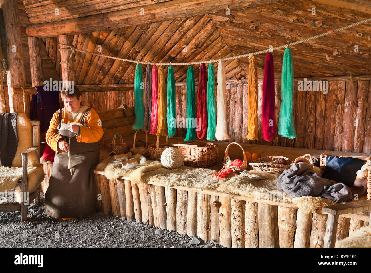 Reenactor in period costume surrounded by variously coloured yarns and handspinning a length of yarn using a drop spindle, Norstead Viking Village and Port of Trade, L'Anse aux Meadows, Newfoundland, Canada Stock Photo