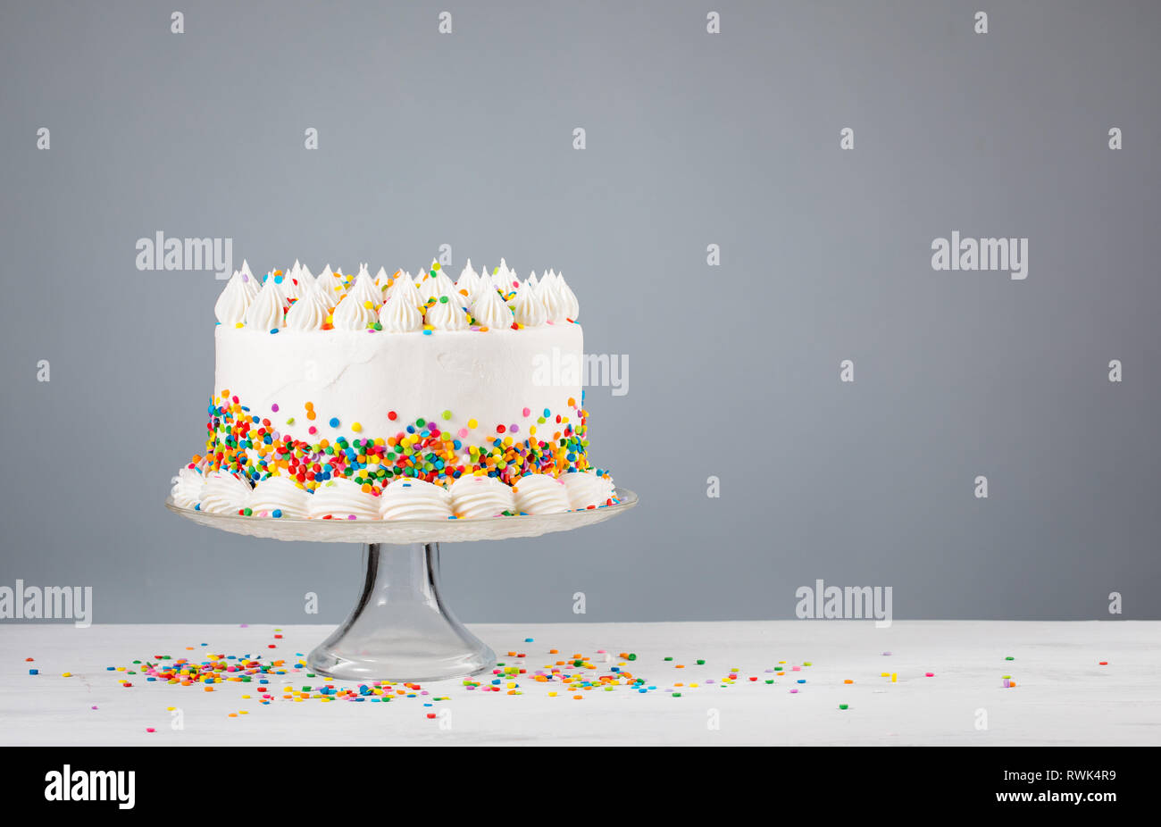White Birthday cake with colorful Sprinkles and sparkler over a neutral  background Stock Photo - Alamy