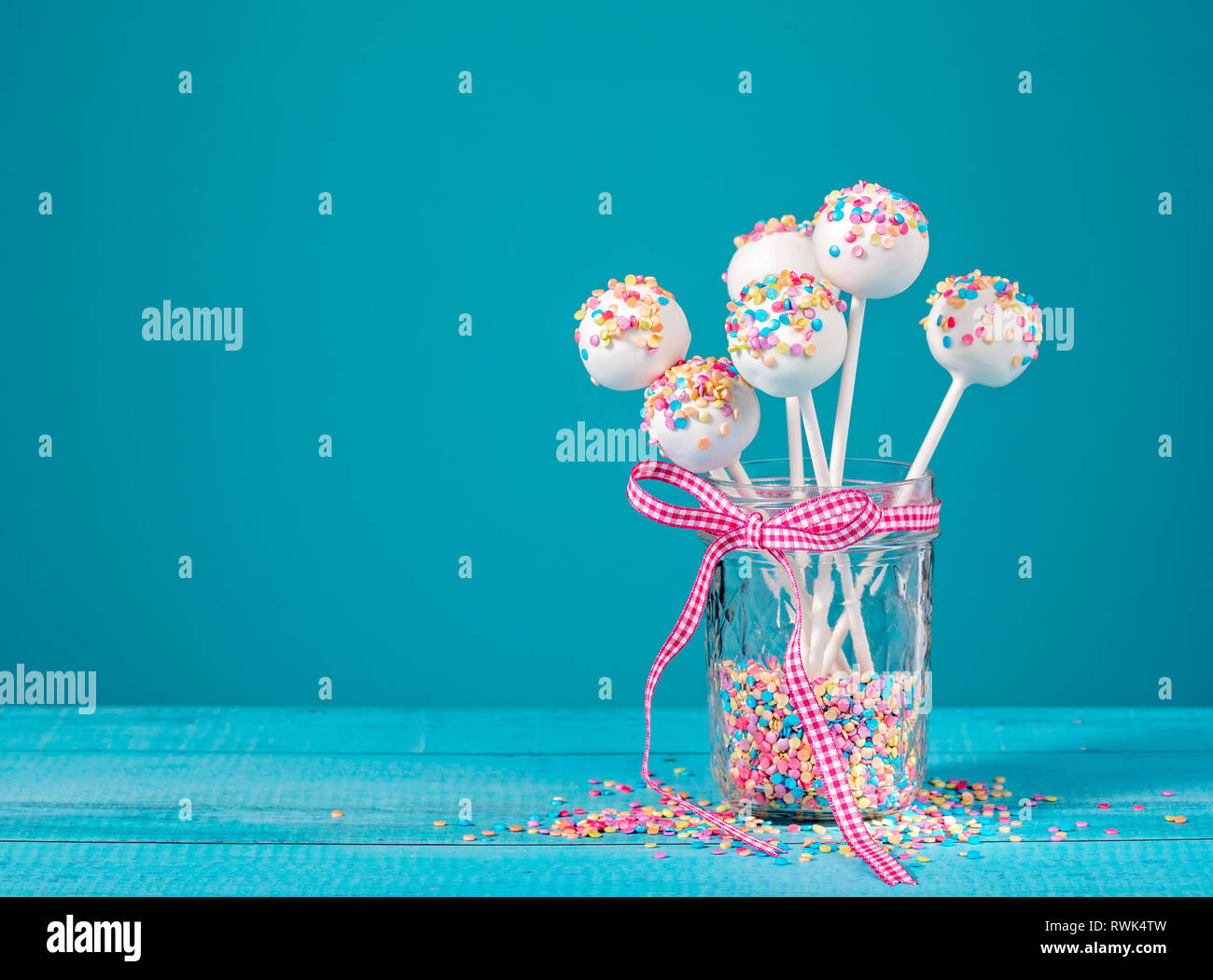 Vanilla cake pops with colorful sprinkles in a cute jar over a blue background. Stock Photo