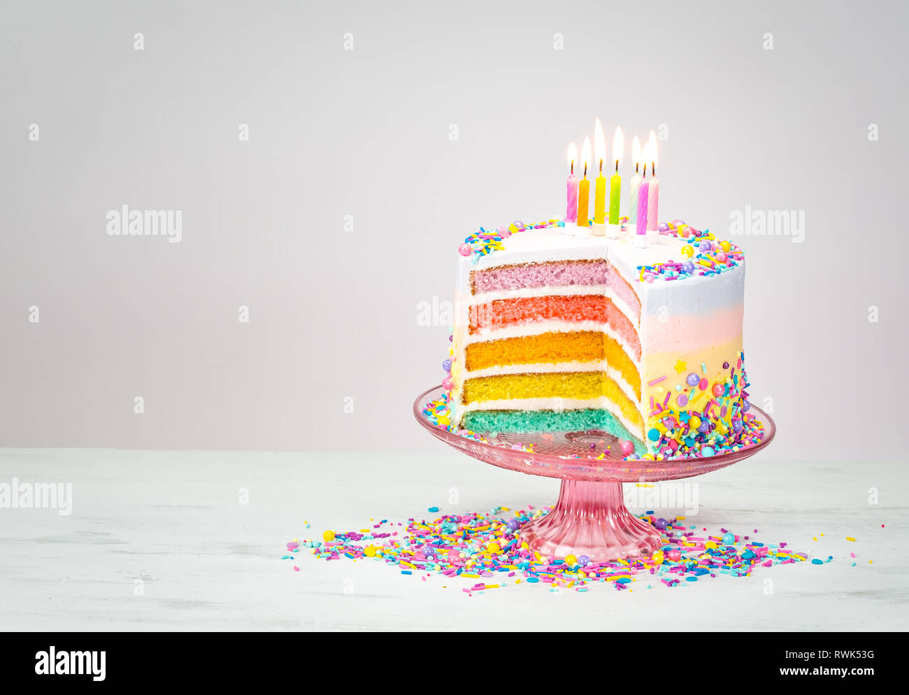 Colorful rainbow layered Birthday cake with lit candles and sprinkles ...