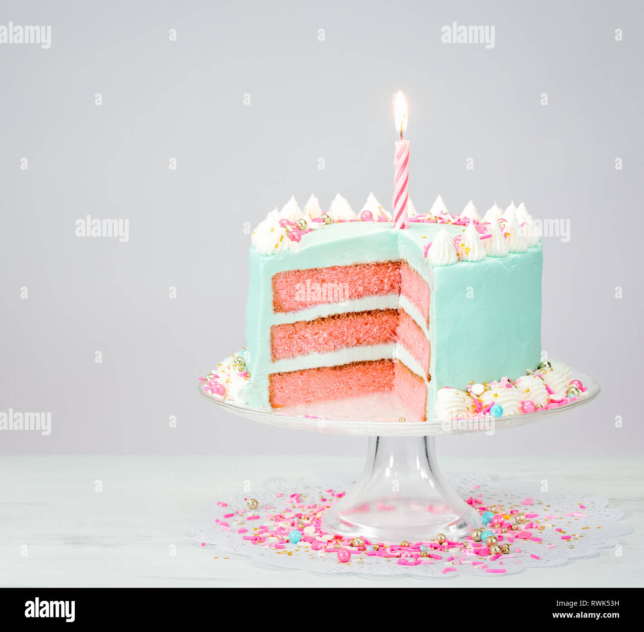 Pastel blue birthday cake over white background with pink layers and sprinkles. Stock Photo