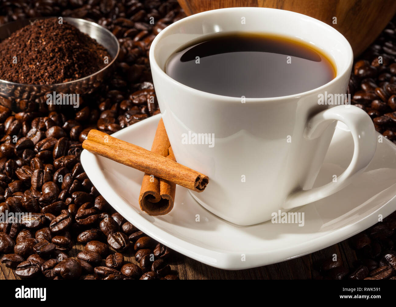 Close-up of a Black Coffee in white Coffee cup with cinnamon and whole and freshly ground beans. Stock Photo