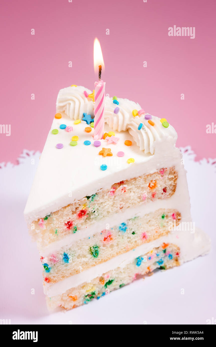 Slice of Birthday Cake with colorful sprinkles and lit candle Stock Photo