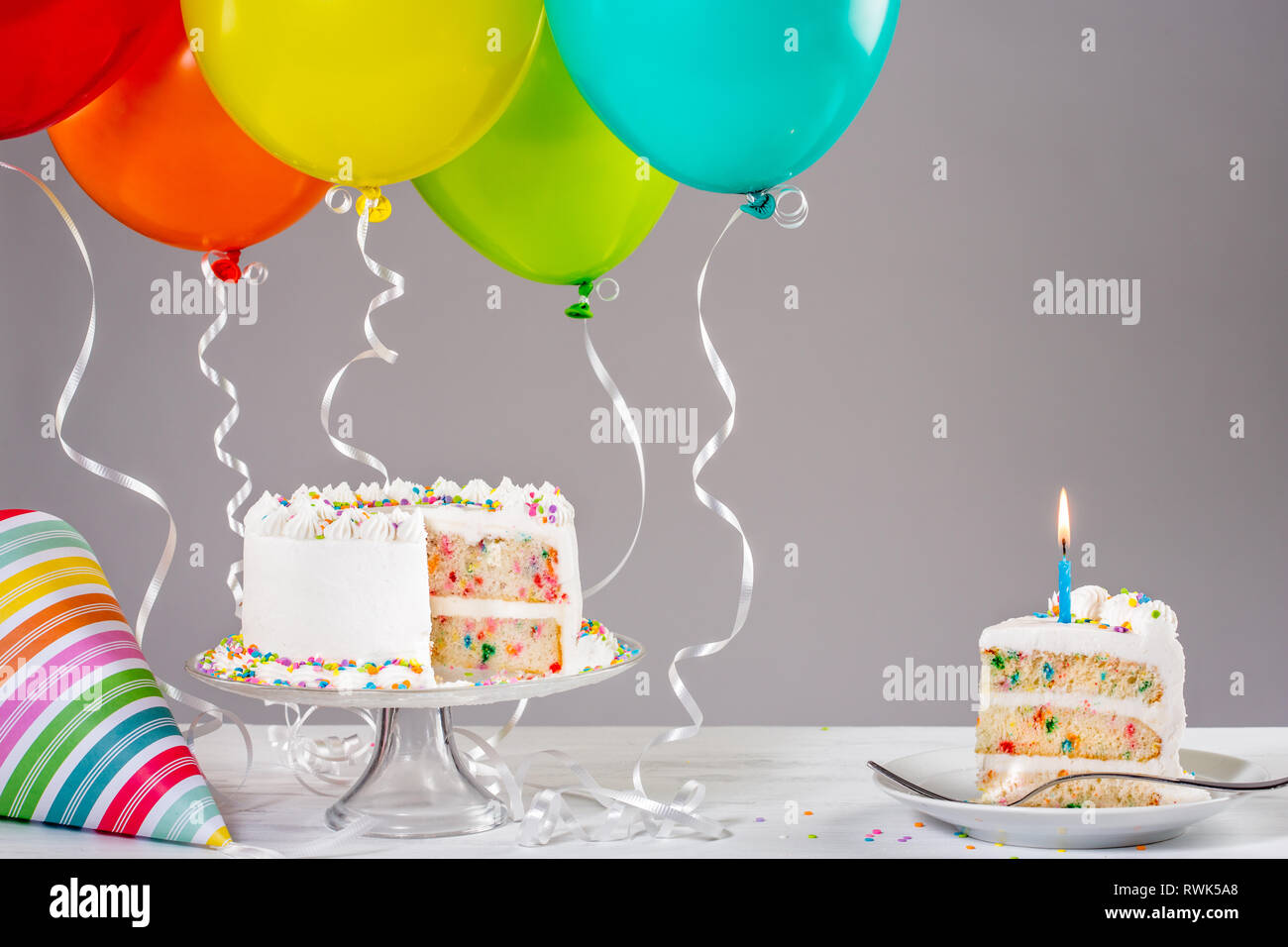 White Buttercream birthday cake with colorful balloons and hat. Stock Photo