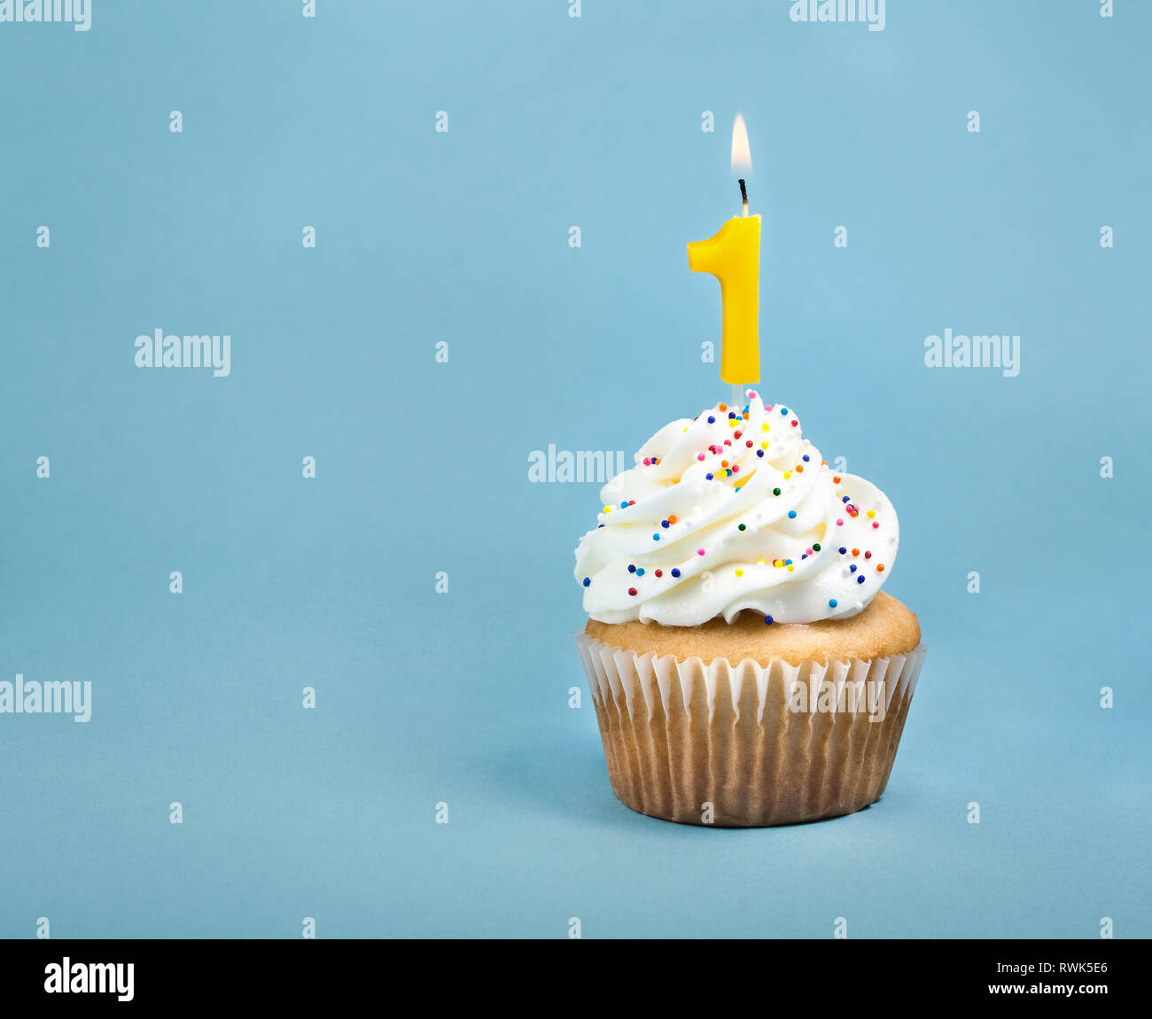 A birthday cup cake with buttercream icing,  sprinkles and a lit number one birthday candle. Stock Photo