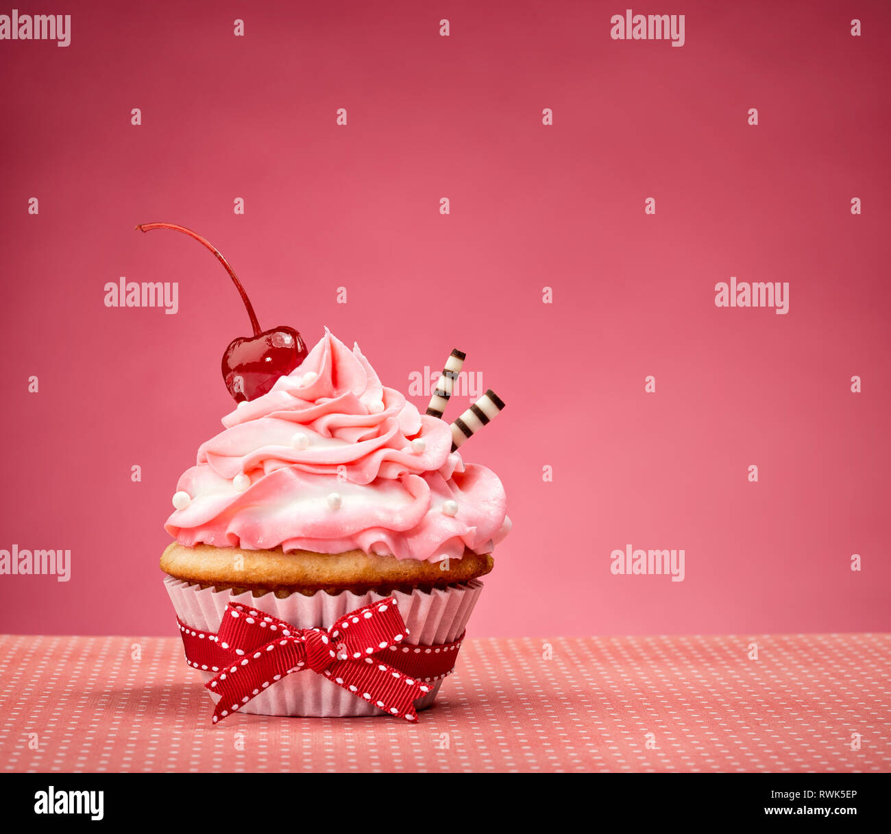 Cupcake with pink buttercream icing and a cherry on top. Stock Photo