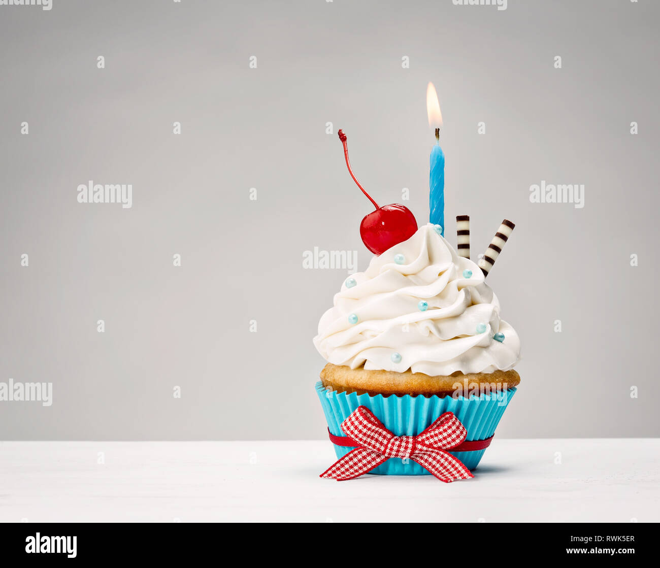 Cupcake with vanilla buttercream icing, birthday candle and a cherry on top. Stock Photo