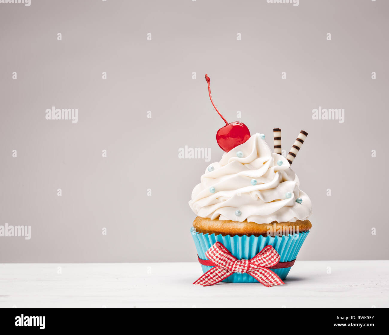 Vanilla buttercream cupcake with a cherry on top over a light grey background. Stock Photo