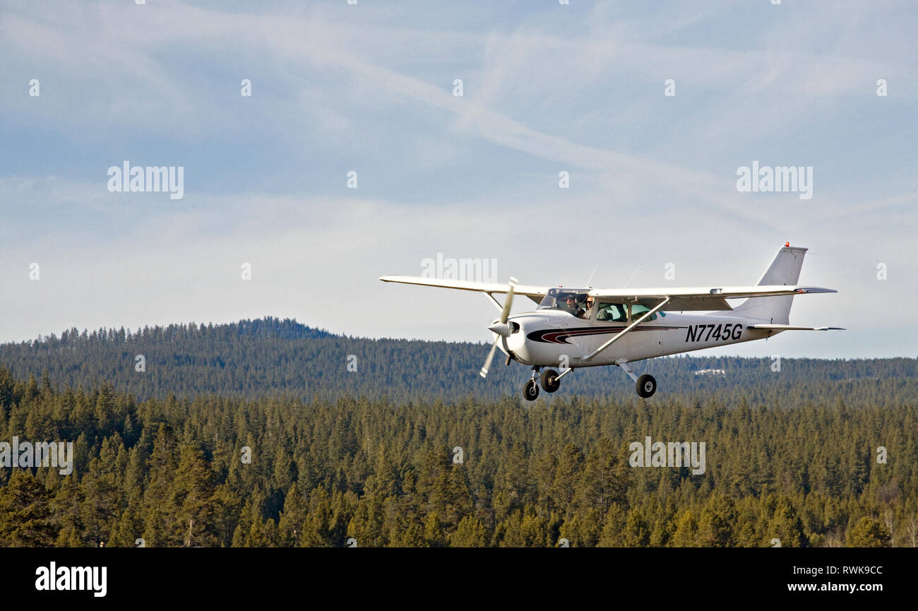 A small Cessna aircraft practices touch and go landings on an airstrip in the Cascade Mountains, Oregon Stock Photo