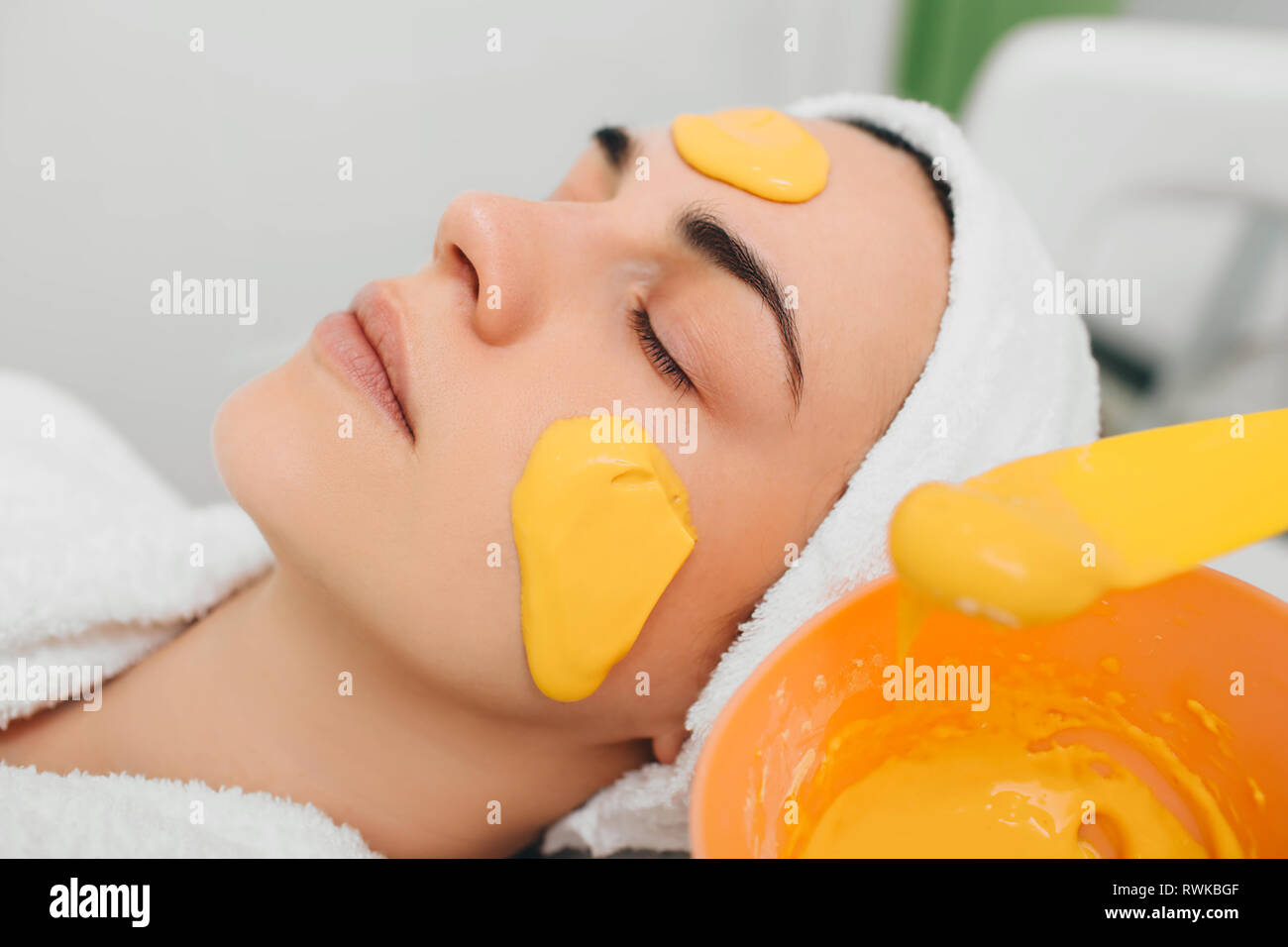 Beautician applying facial mask with orange extract on beautiful female face Stock Photo