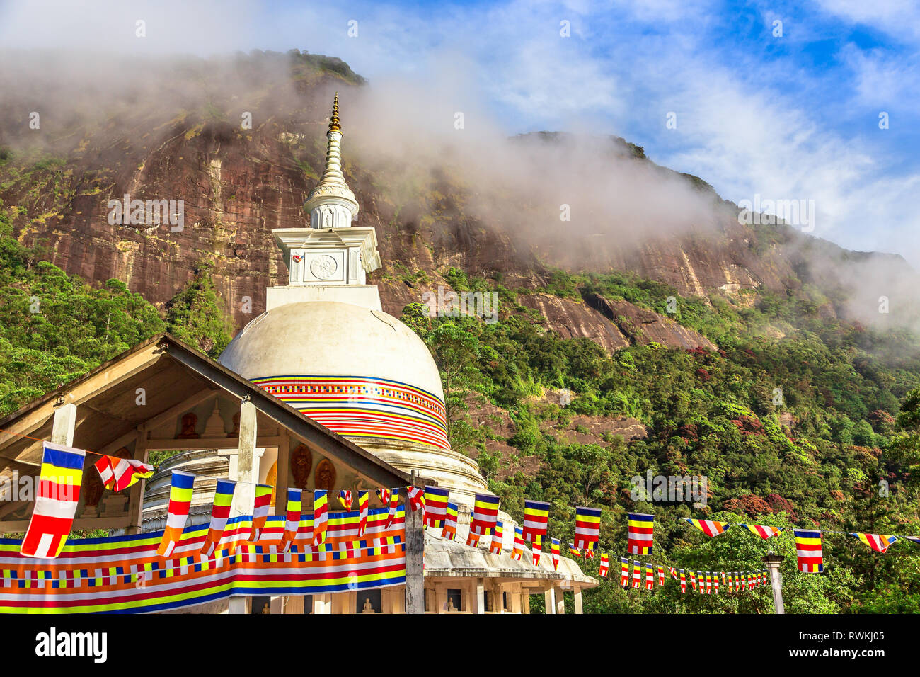 Colorful buddhist flags with stupa temple, green mountains and blue sky in the background, on the way to the top of Adam's peak, Sri Lanka Stock Photo