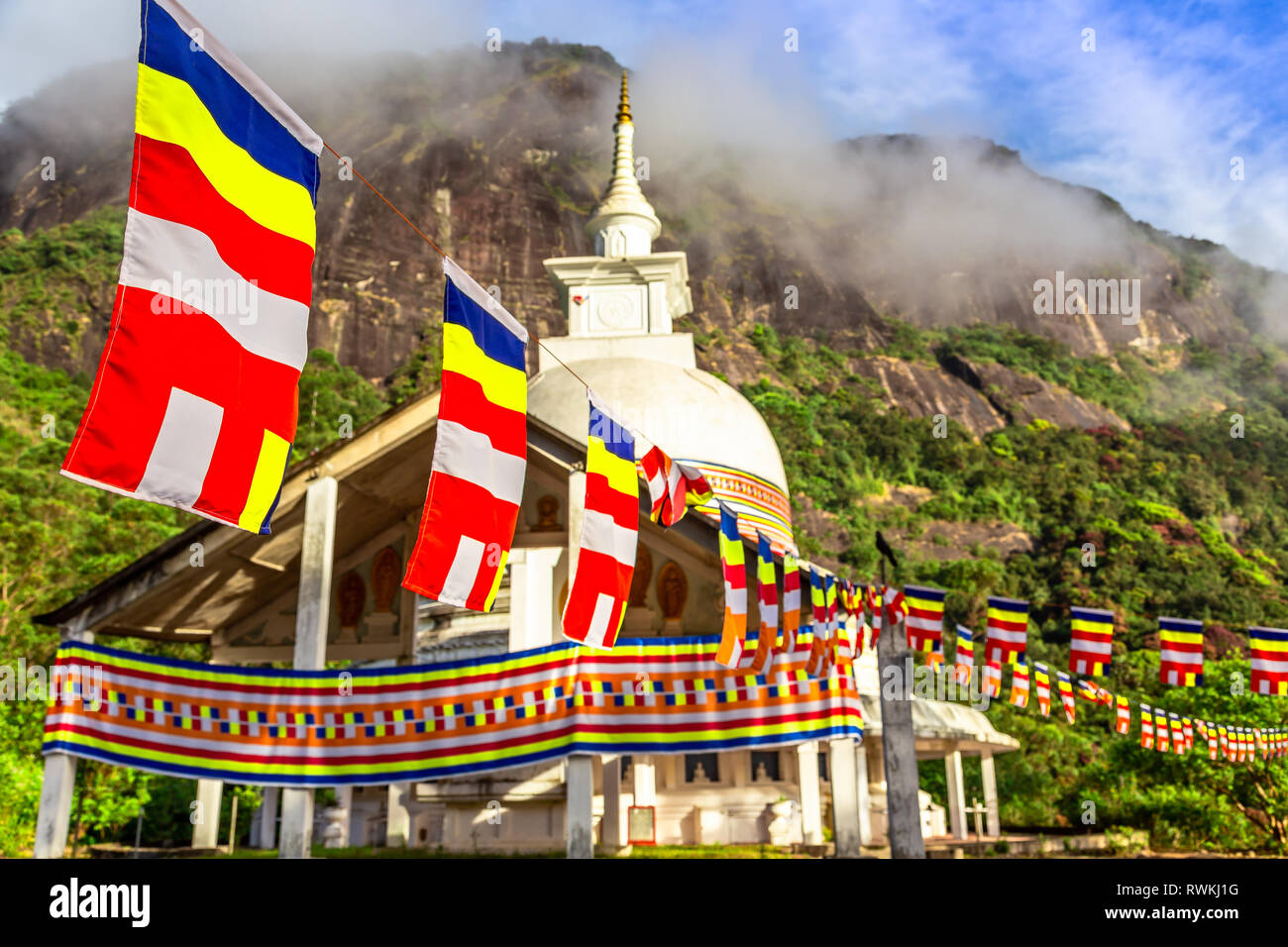 Colorful buddhist flags with stupa temple, green mountains and blue sky in the background, on the way to the top of Adam's peak, Sri Lanka Stock Photo