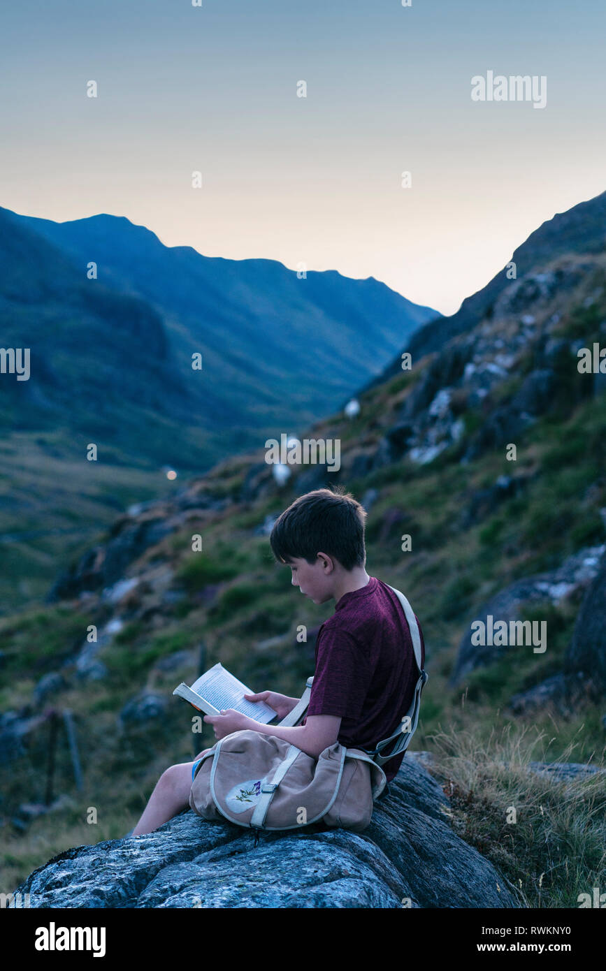 Boy reading book on hilltop, Snowdonia, Llanberis, Gwynedd, UK Stock Photo