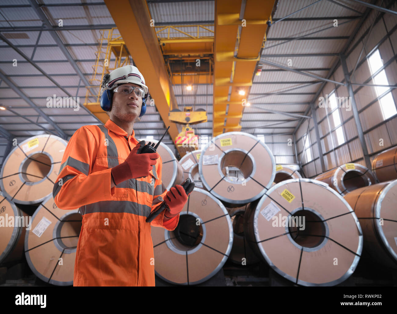 Composite image of worker with rolls of steel in port depot Stock Photo