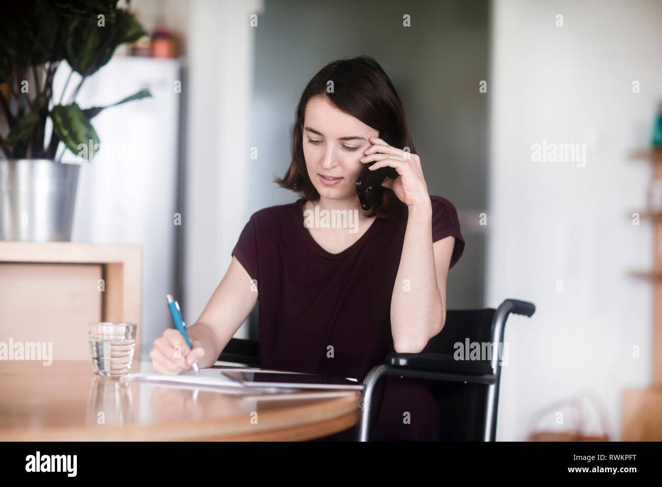 Woman in wheelchair using cellphone and taking notes Stock Photo