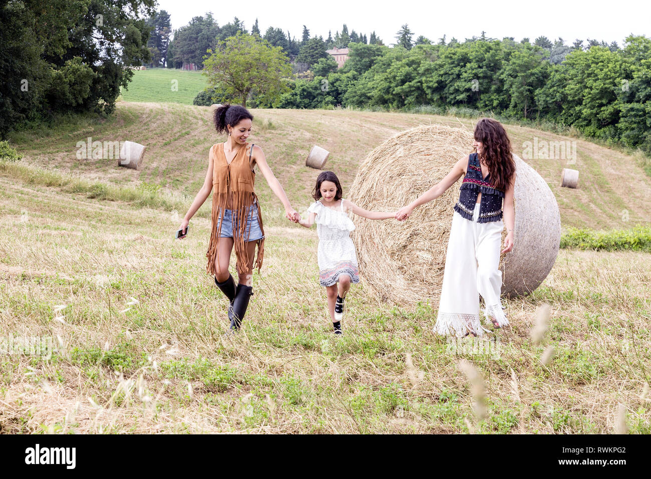 Friends and girl in field of hay bales, Città della Pieve, Umbria, Italy Stock Photo