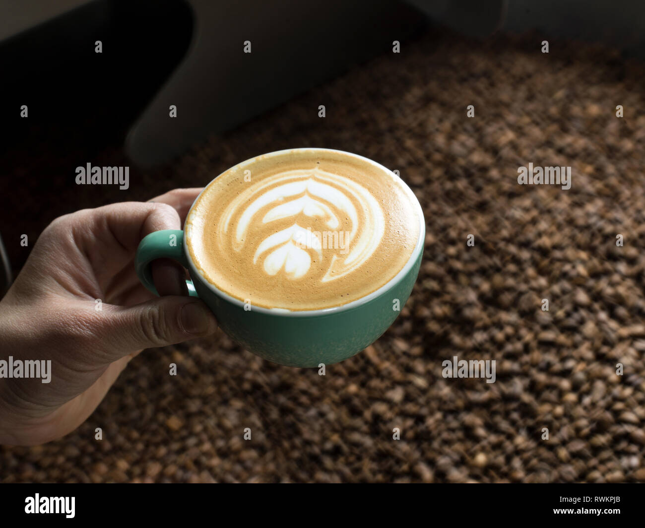 Hand holding cup of coffee over coffee roaster Stock Photo