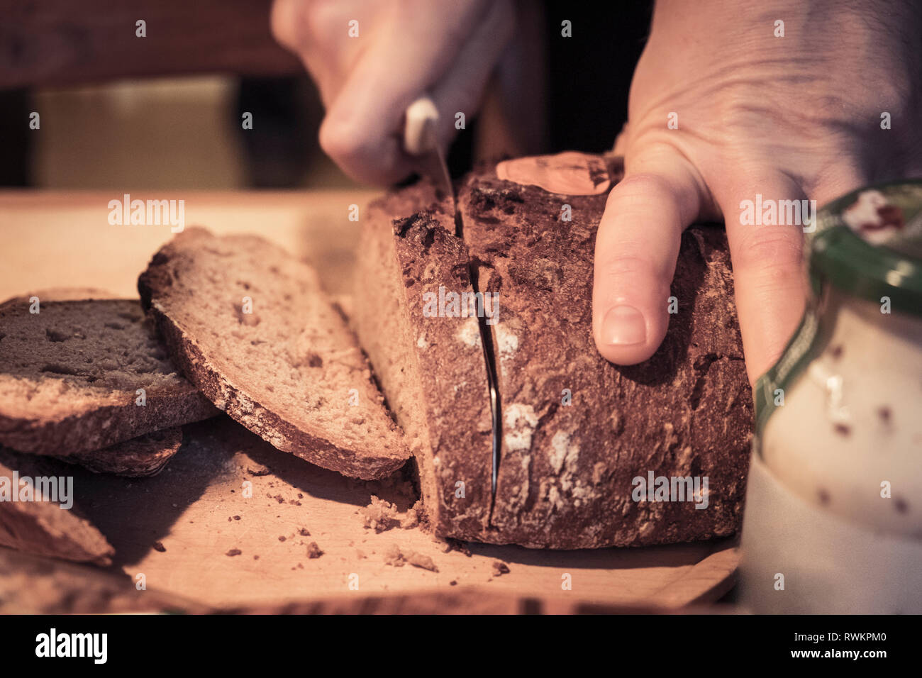 Man slicing rustic brown loaf, close up of hand Stock Photo