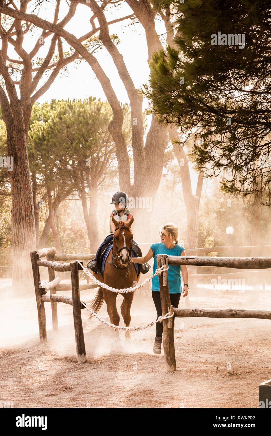 Mother leading horse riding daughter in paddock, Portoferraio, Tuscany, Italy Stock Photo