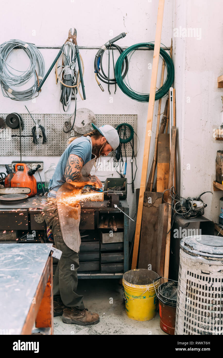 Axe maker using steel grinder in workshop Stock Photo