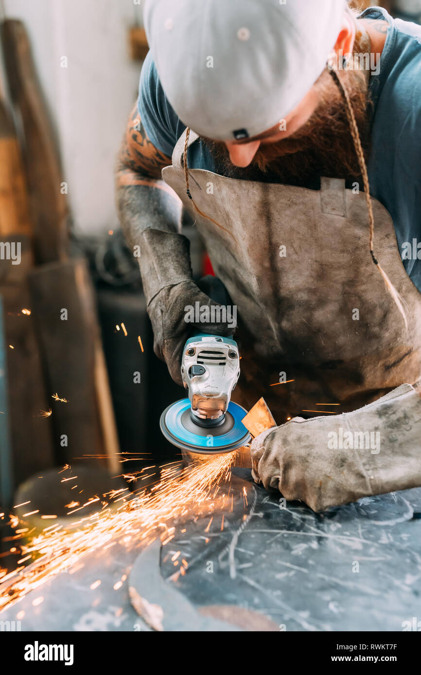 Axe maker using steel grinder in workshop Stock Photo