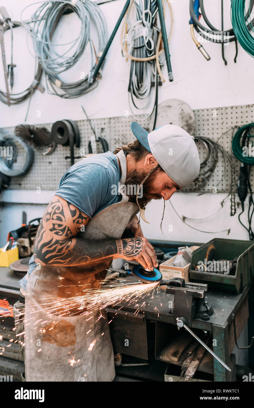 Axe maker using steel grinder in workshop Stock Photo