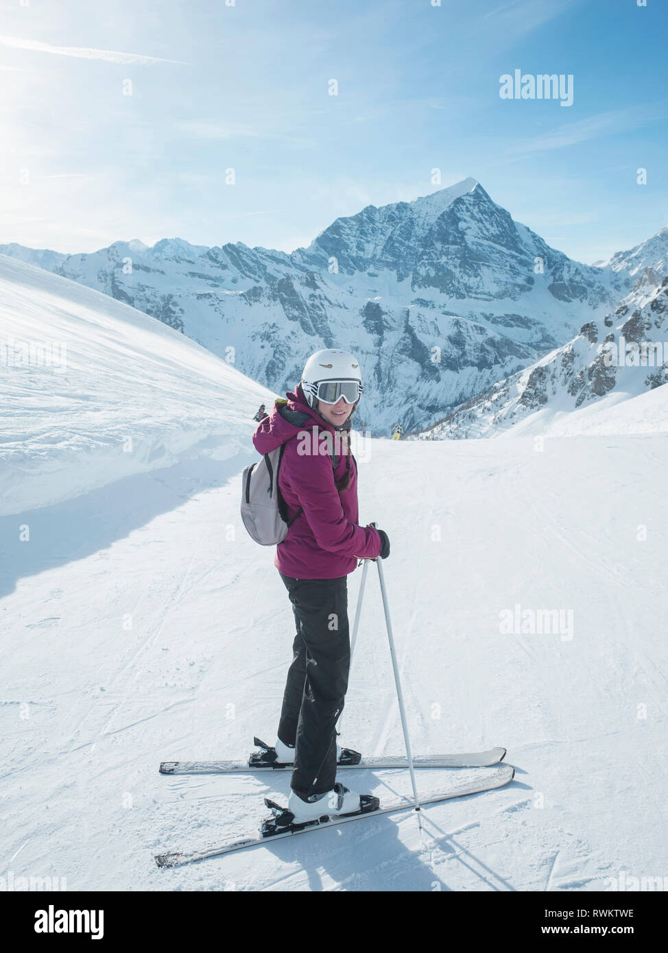 Young woman skier wearing helmet and ski goggles looking back in snow covered landscape,  Alpe Ciamporino, Piemonte, Italy Stock Photo