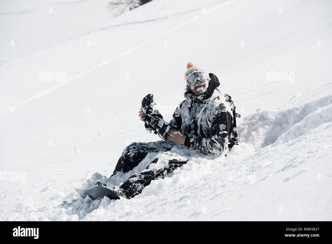 Male snowboarder covered in snow sitting on mountainside, Alpe-d'Huez, Rhone-Alpes, France Stock Photo