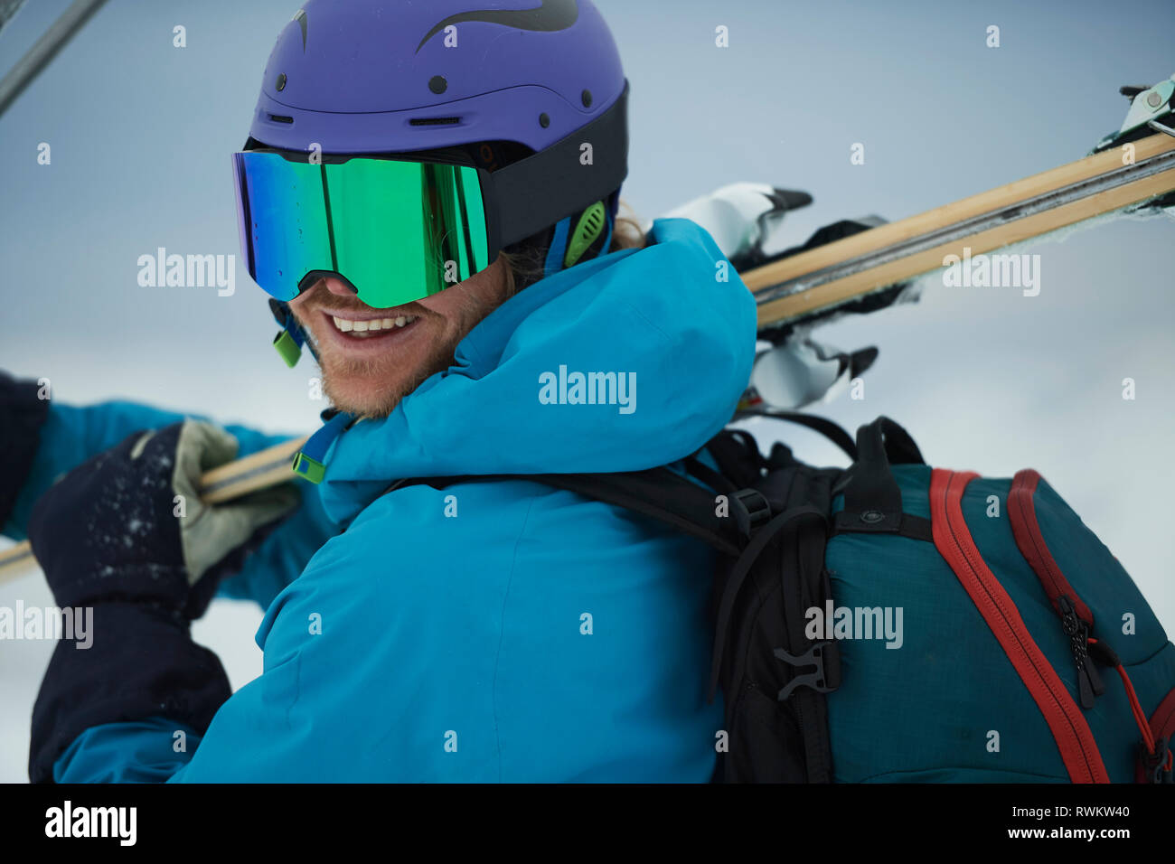 Male skier carrying skis looking over shoulder, portrait, Alpe-d'Huez, Rhone-Alpes, France Stock Photo