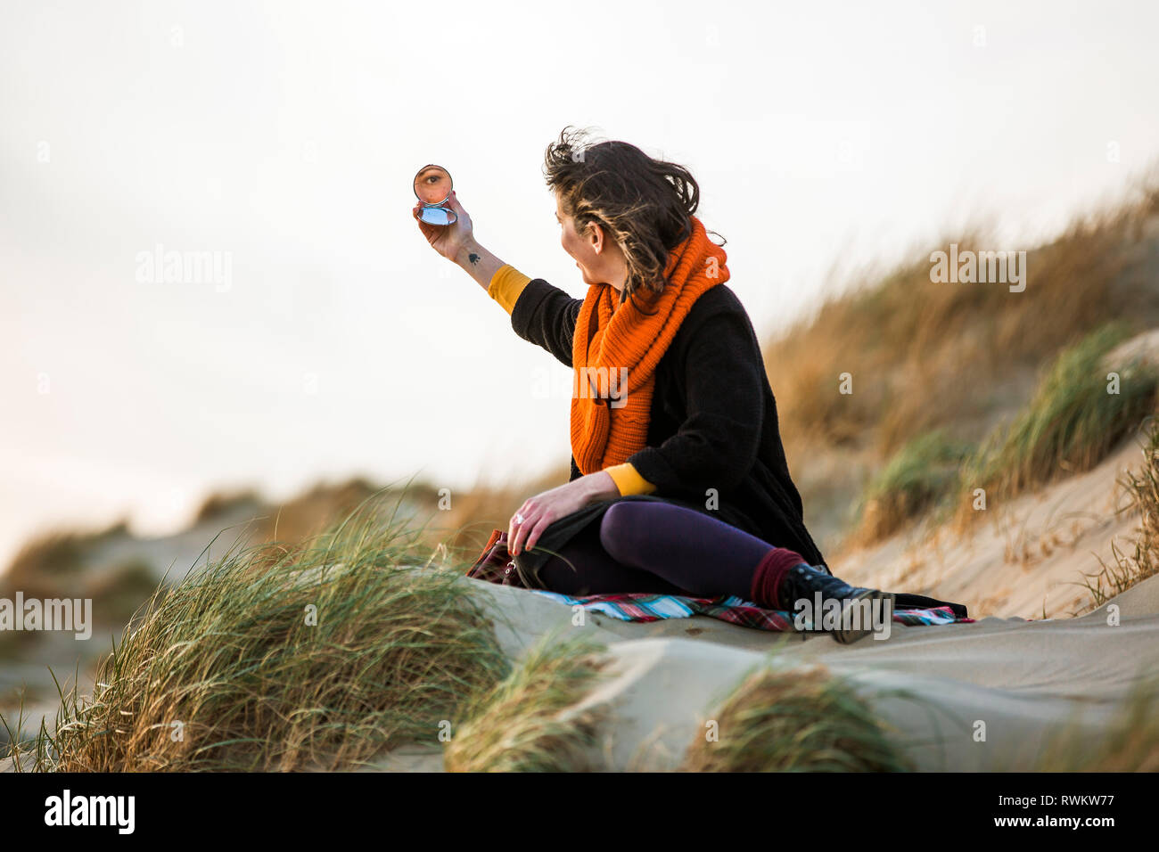 Woman looking at compact mirror on beach Stock Photo