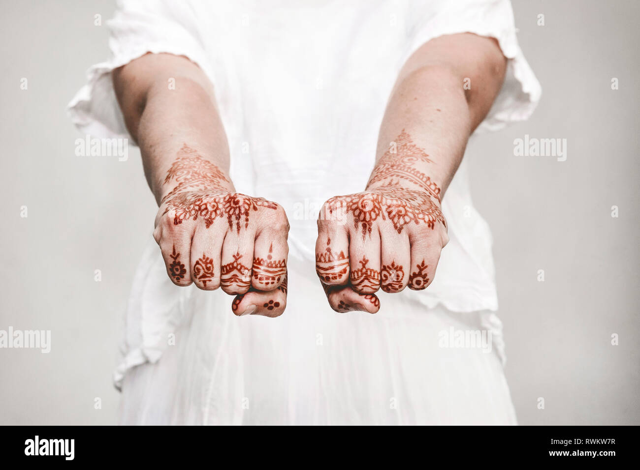 Woman in white dress with henna tattoo on fists Stock Photo