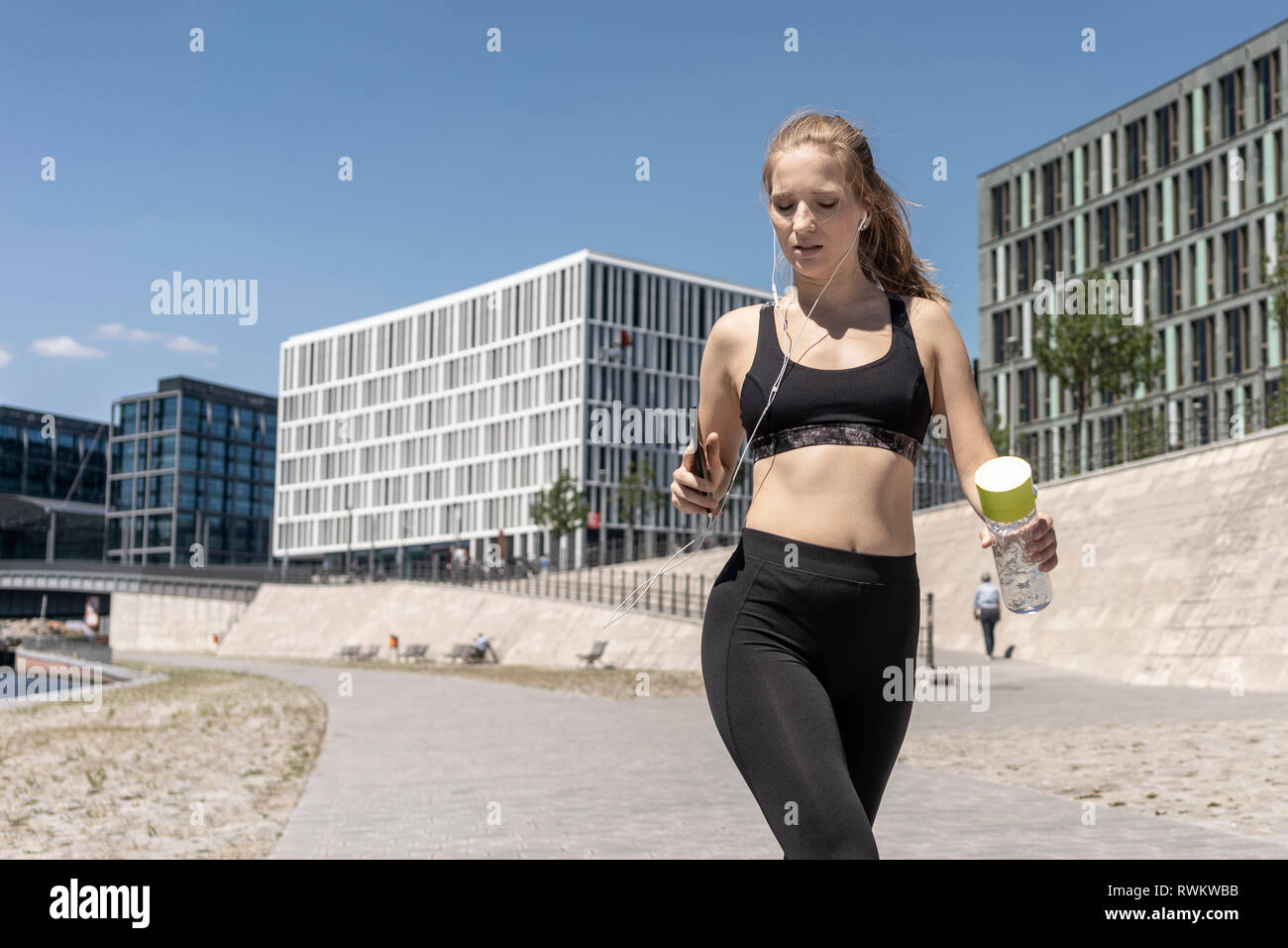 Young woman running and using smartphone in city, Berlin, Germany Stock Photo